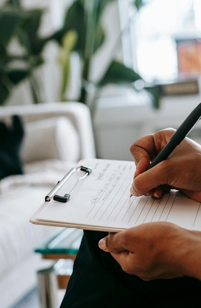 crop ethnic psychologist writing on clipboard during session